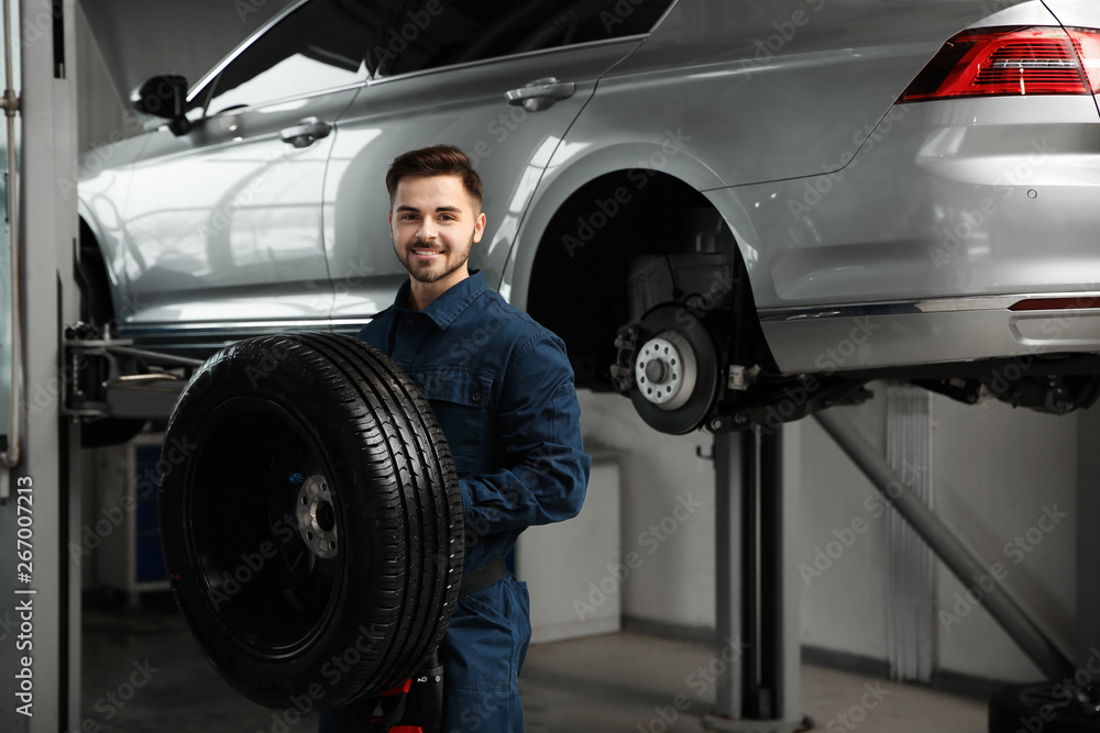 Technician with car wheel in automobile repair shop