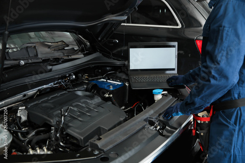 Technician checking car with laptop at automobile repair shop