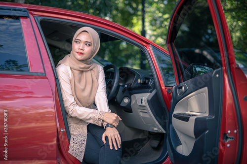 portrait of young muslim woman in hijab sitting on car seat with opened door. Female driver concept. © SafwanAbdRahman