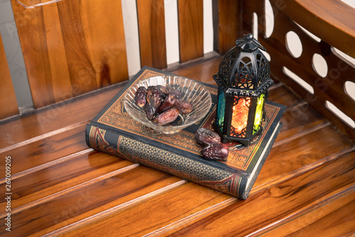 Islamic, ramadan and praying concept. Arabic lantern, dates or kurma with arabic book known as kitab or Quran on classic shine wood background, copy space, selective focus. photo