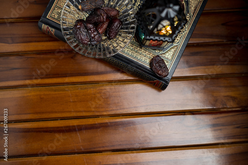Islamic, ramadan and praying concept. Arabic lantern, dates or kurma with arabic book known as kitab or Quran on classic shine wood background, copy space, selective focus.
