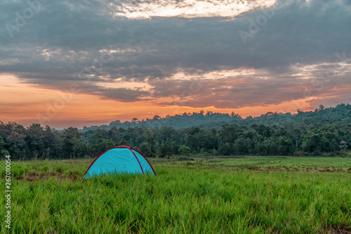 landscape scenery of camping tent on grass field with background of forest and mountains and sunrising sky in natural park