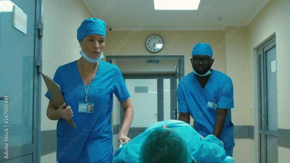 Mixed ethnic medical stuff carrying patient on medical gurney through hospital corridor Mixed ethnic medical stuff carrying patient on medical gurney through hospital corridor