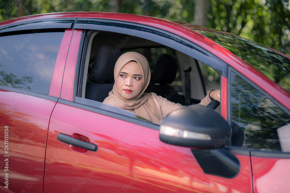 Young Muslim woman looking through car window with face expression, female drivers concept.