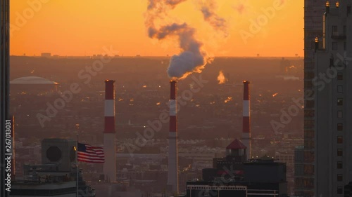 Close up American flag waves beneath the industrial chimney emitting smoke harmful smoke from a power plant on the outskirts of new York
