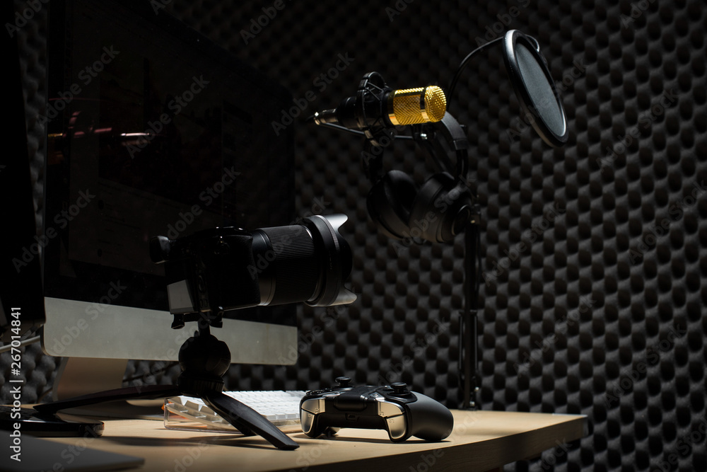 Microphone Condenser, gold mic hang over sound absorbing wall room with wave monitor keyboard mouse game pad controller and headphone in dark audio studio, low exposure lighting background copy space Microphone Condenser, gold mic hang over sound absorbing wall room with wave monitor keyboard mouse game pad controller and headphone in dark audio studio, low exposure lighting background copy space