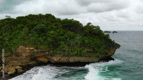 Aerial drone shot of the mystical island with steep cliffs. Beautiful scenery opening behind the island. Big waves hit the bottom of the island. photo