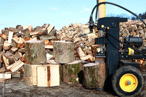 Yellow and black log splitter on end to split vertically with blocks, heap and woodpile  photo