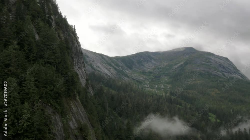 A misty mountain range in an Alaskan fjord reveals depth, rock, and vegetation as the landscape rests against the sky. A misty mountain range in an Alaskan fjord reveals depth, rock, and vegetation as the landscape rests against the sky.