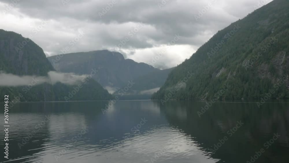 A depth shot of Alaskan misty mountains resting on the water within a fjord. A depth shot of Alaskan misty mountains resting on the water within a fjord.