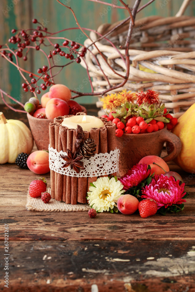 Candle decorated with cinnamon sticks among autumn fruits and flowers.