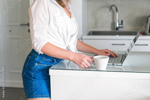 Girl with laptop with cap of coffee on the kitchen. Working home concept