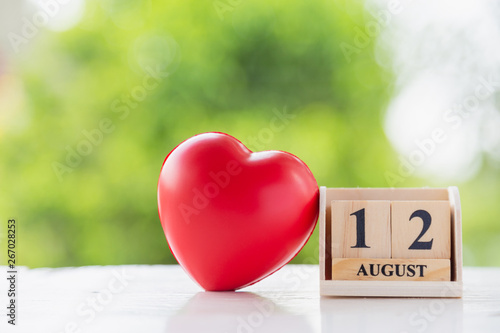 Wooden square block number 12 August with a red heart shape ball on wooden floor