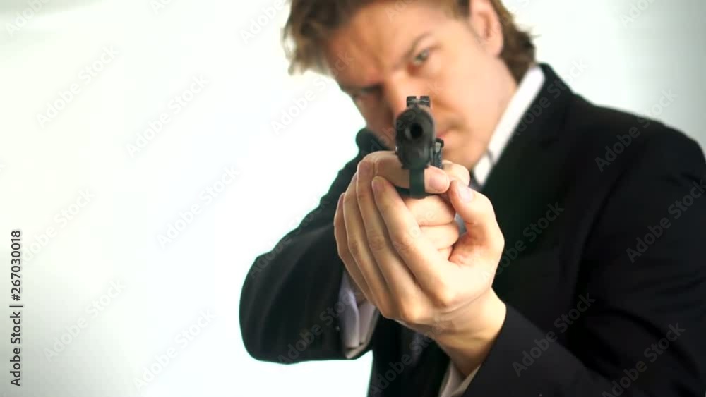 Bodyguard aims down the sights of his pistol and looks at the camera.Man in suit aims his gun. A threatening stance, aiming down the sights of his pistol, police, mafia criminal or mercenary. Focus is Bodyguard aims down the sights of his pistol and looks at the camera.Man in suit aims his gun. A threatening stance, aiming down the sights of his pistol, police, mafia criminal or mercenary. Focus is