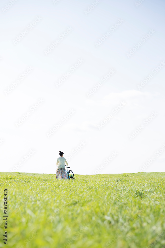 Obraz premium 草原で自転車を押す女性の後姿