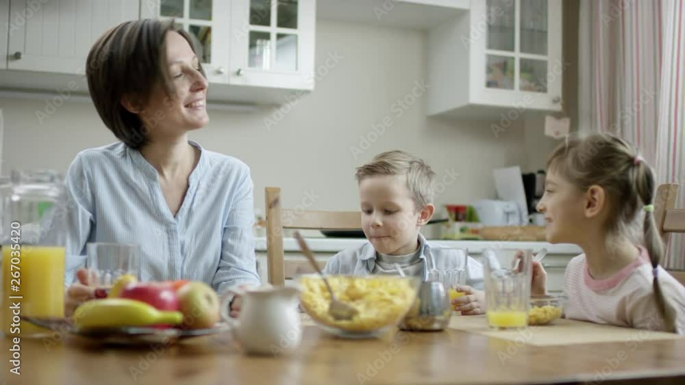 mother communicate during breakfast with her children and put cornflakes from bowl on the plate with a spoon to her daughter