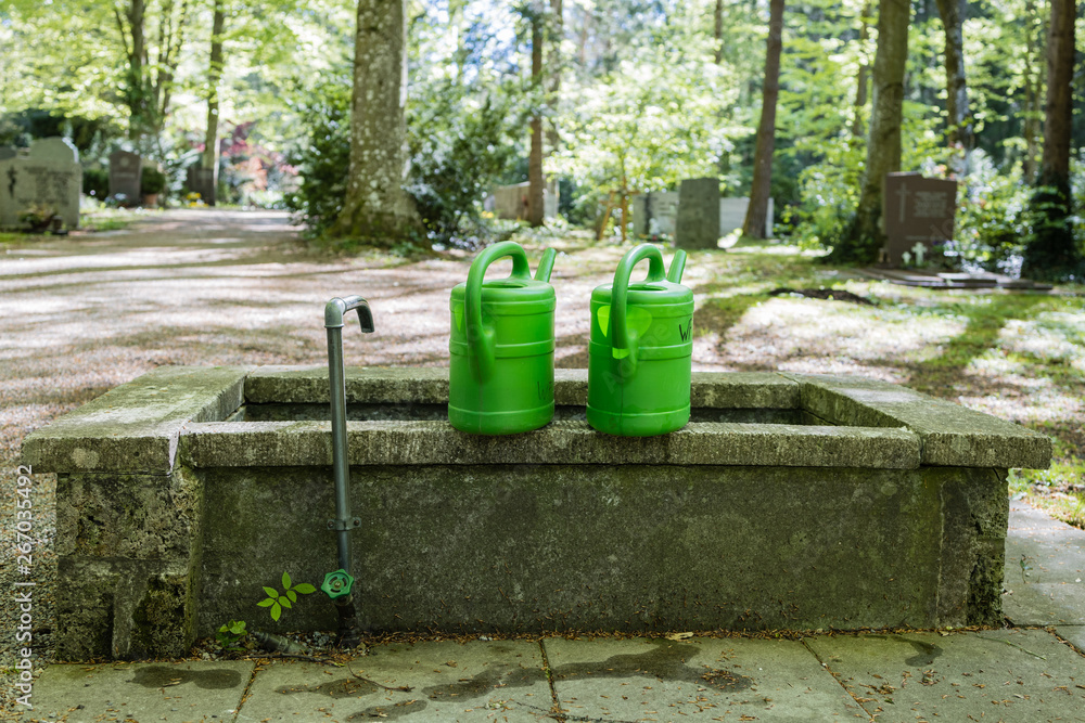 Grüne Giesskanne auf Friedhof an Wasserstelle im Frühling Grüne Giesskanne auf Friedhof an Wasserstelle im Frühling