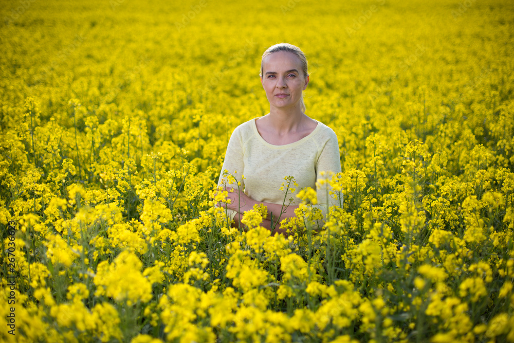 Fototapeta premium Happy woman on blooming rapeseed field in springin yellow blouse.