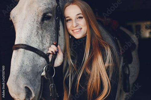 Girl with a horse. Woman in a ranch. Blonde in a black sweater