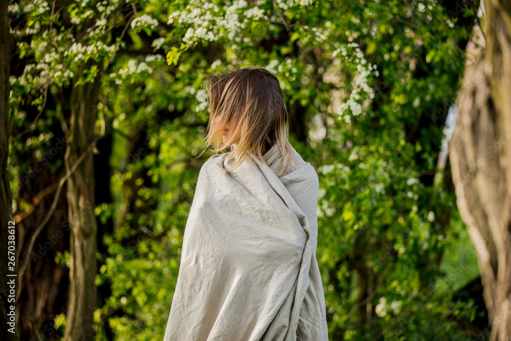 a young girl wrapped in a blanket is standing in a meadow near the trees during sunset a young girl wrapped in a blanket is standing in a meadow near the trees during sunset