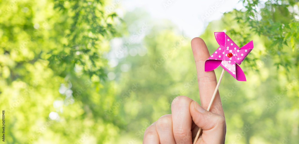 childhood, summer and body part concept - close up of hand holding pinwheel toy over green natural background