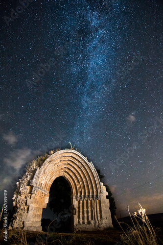 Stars and Milky Way with the ruins of St. Michael arch in Sasamon, Burgos, (Spain) in foreground
