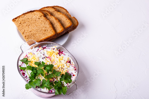 Traditional Russian layered betroot and herring salad (under a fur coat) in glass jar, white background, selective focus photo