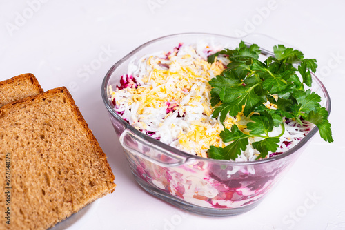 Traditional Russian layered betroot and herring salad (under a fur coat) in glass jar, white background, selective focus photo