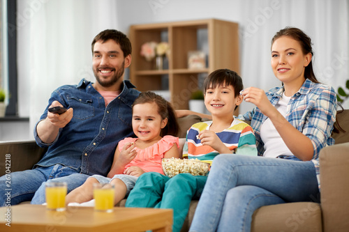 family, leisure and people concept - happy mother, father, son and daughter with popcorn watching tv at home