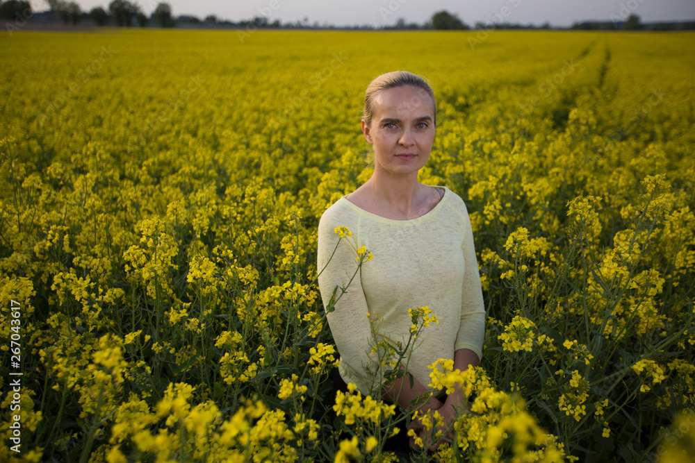 Fototapeta premium Happy woman on blooming rapeseed field in springin yellow blouse.