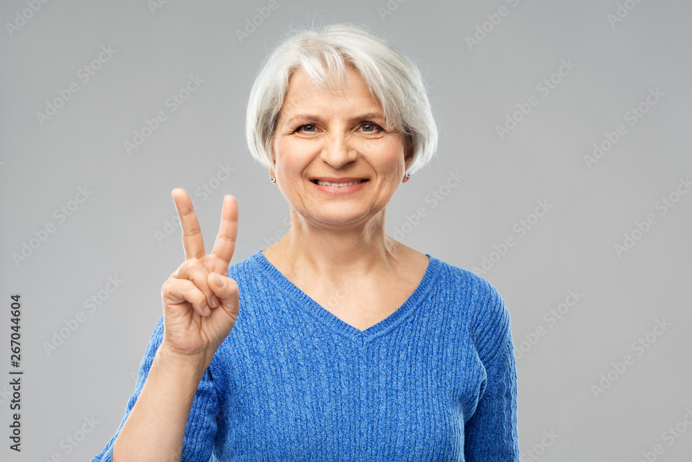 gesture and old people concept - portrait of smiling senior woman in blue sweater showing peace over grey background gesture and old people concept - portrait of smiling senior woman in blue sweater showing peace over grey background