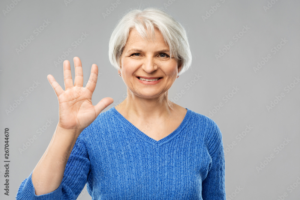 gesture and old people concept - portrait of smiling senior woman in blue sweater showing palm or five fingers over grey background gesture and old people concept - portrait of smiling senior woman in blue sweater showing palm or five fingers over grey background