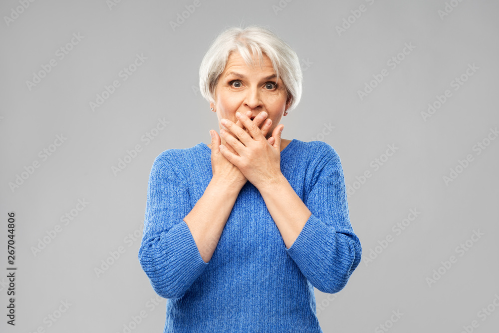 emotion, expression and old people concept - portrait of confused senior woman in blue sweater covering her mouth by hands over grey background emotion, expression and old people concept - portrait of confused senior woman in blue sweater covering her mouth by hands over grey background