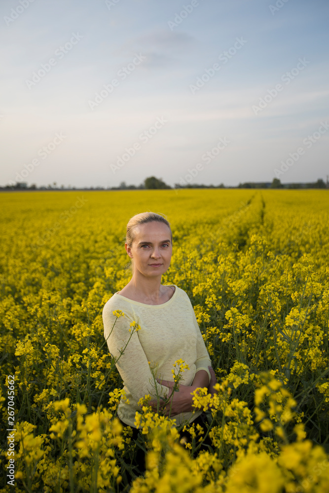 Fototapeta premium Happy woman on blooming rapeseed field in springin yellow blouse.