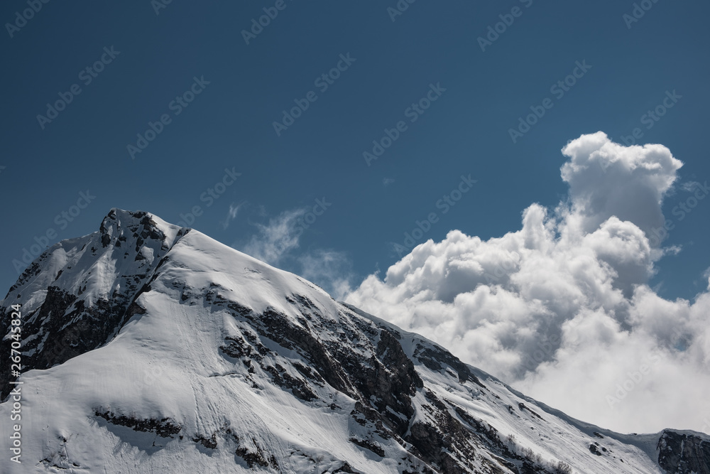 Aerial photography. Snow-capped mountains. Clouds in the blue sky. The top of the mountain Aibga, Sochi. Ski resort Krasnaya Polyana.