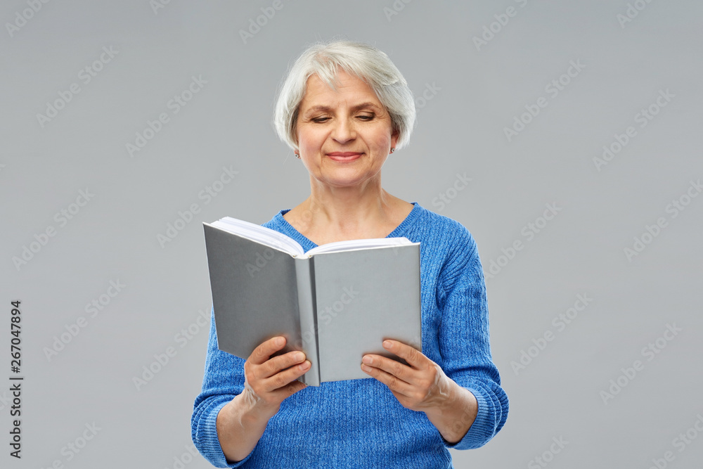 wisdom, literature and old people concept - smiling senior woman reading book over grey background