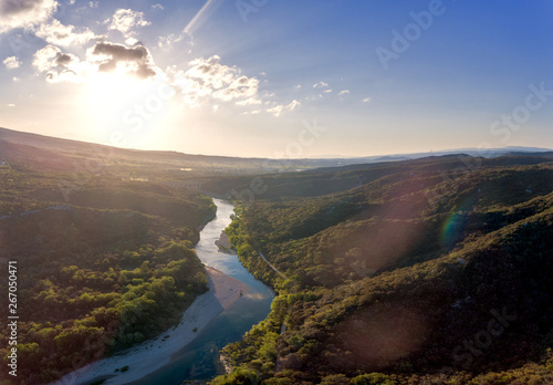 Stunning aerial drone shot of the Rhone river at sunrise. The river reflects the early morning sun and the river gorge is forested and green. An old roman bridge can be see in the distance. photo