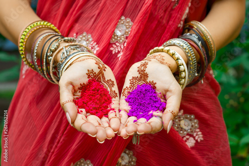Beautiful woman wear traditional Indian wedding red sari dress hold in hands with henna tattoo and bracelets colorful pink violet Holi dust powder paint. Happy holiday summer culture festival concept