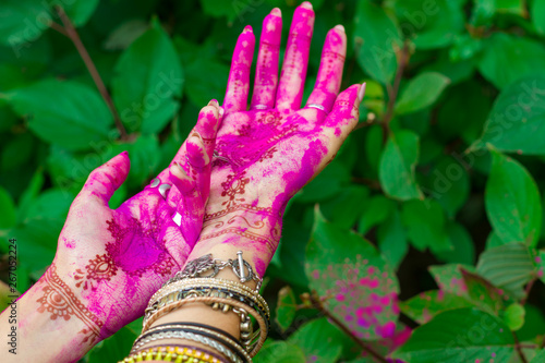 Woman smeared hands with henna tattoo and bracelets jewelry colorful pink violet Holi dust powder paint Happy traditional Indian wedding holiday summer culture festival concept Green leaves background