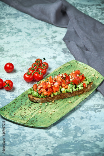 On a green plate of brusket with tomatoes and avocado. Light gray textured background. Beautiful serving of dishes. Restaurant menu photo