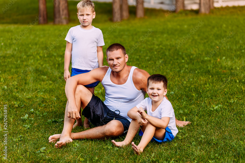 father and two children sit on the green lawn in the summer. A man and two young sons of a preschooler in the summer father and two children sit on the green lawn in the summer. A man and two young sons of a preschooler in the summer