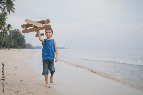 Little boy playing with cardboard toy airplane on the beach