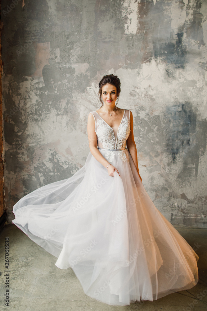 a young beautiful wedding bride in a beautiful long dress is standing in a loft-style apartment near the window a young beautiful wedding bride in a beautiful long dress is standing in a loft-style apartment near the window
