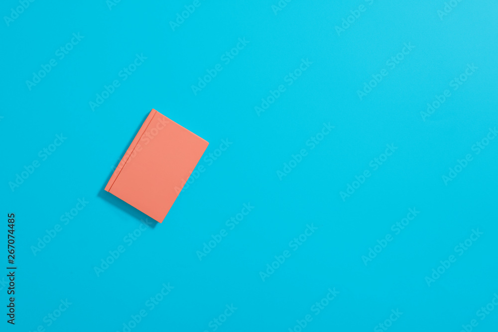 Orange hardcover notebook lying flat and offset on a pastel blue background with copy space and room for text with a left sided composition on a horizontal image. Orange hardcover notebook lying flat and offset on a pastel blue background with copy space and room for text with a left sided composition on a horizontal image.