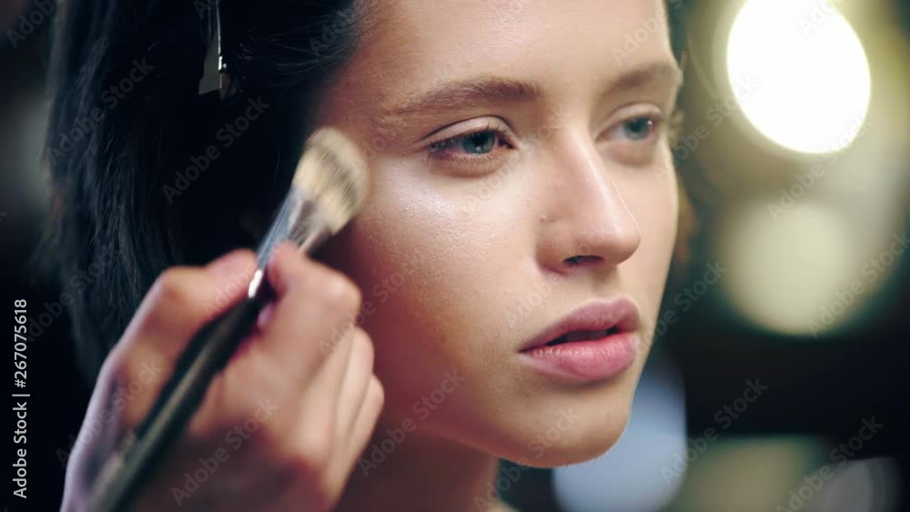 cropped view of makeup artist applying shimmering highlighter on model face with cosmetic brush cropped view of makeup artist applying shimmering highlighter on model face with cosmetic brush