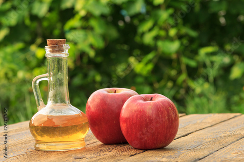 Apple vinegar in glass bottle and fresh red apples on wooden boards