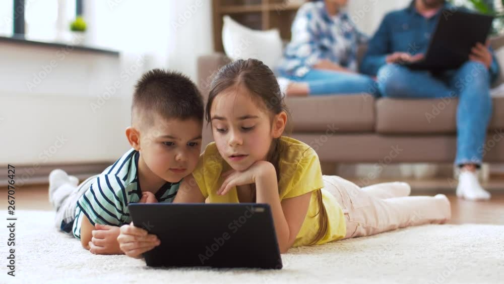 childhood, technology and family concept - little brother and sister with tablet pc computer lying on floor at home childhood, technology and family concept - little brother and sister with tablet pc computer lying on floor at home