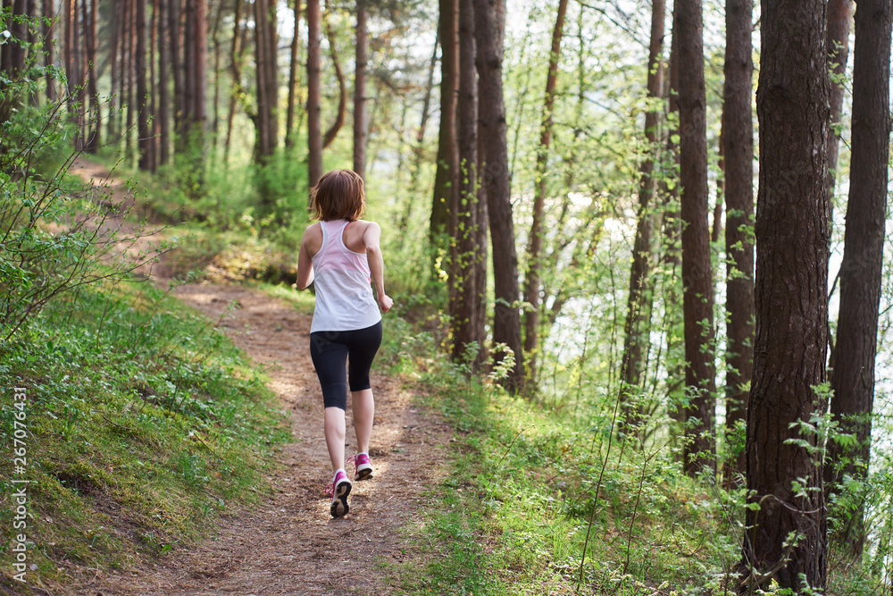 Obraz premium Athletic young woman in pink sneakers run in spring forest