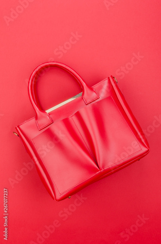 Bright summer fashion ladies accessories. Stylish red leather handbag or shopper bag turned on its side on a red background. Top View. Flat Lay. Copy Space. Mock Up.