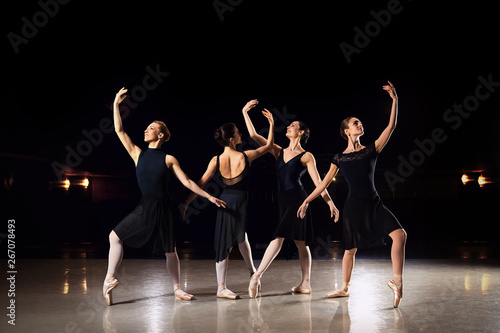 A group of ballerinas are dancing on the scene against a black background.